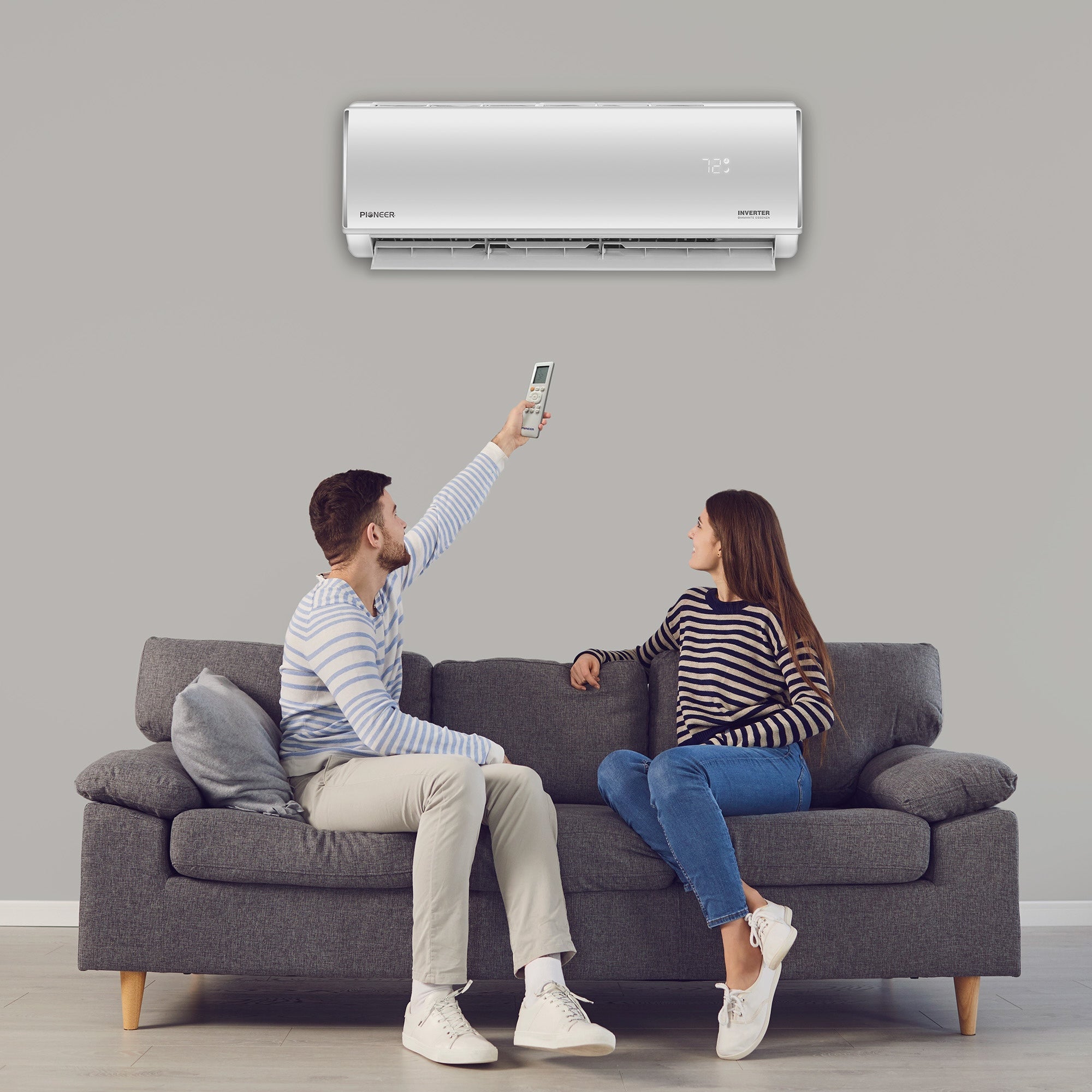 Man and woman sitting on a couch using a remote control to operate an air conditioner.