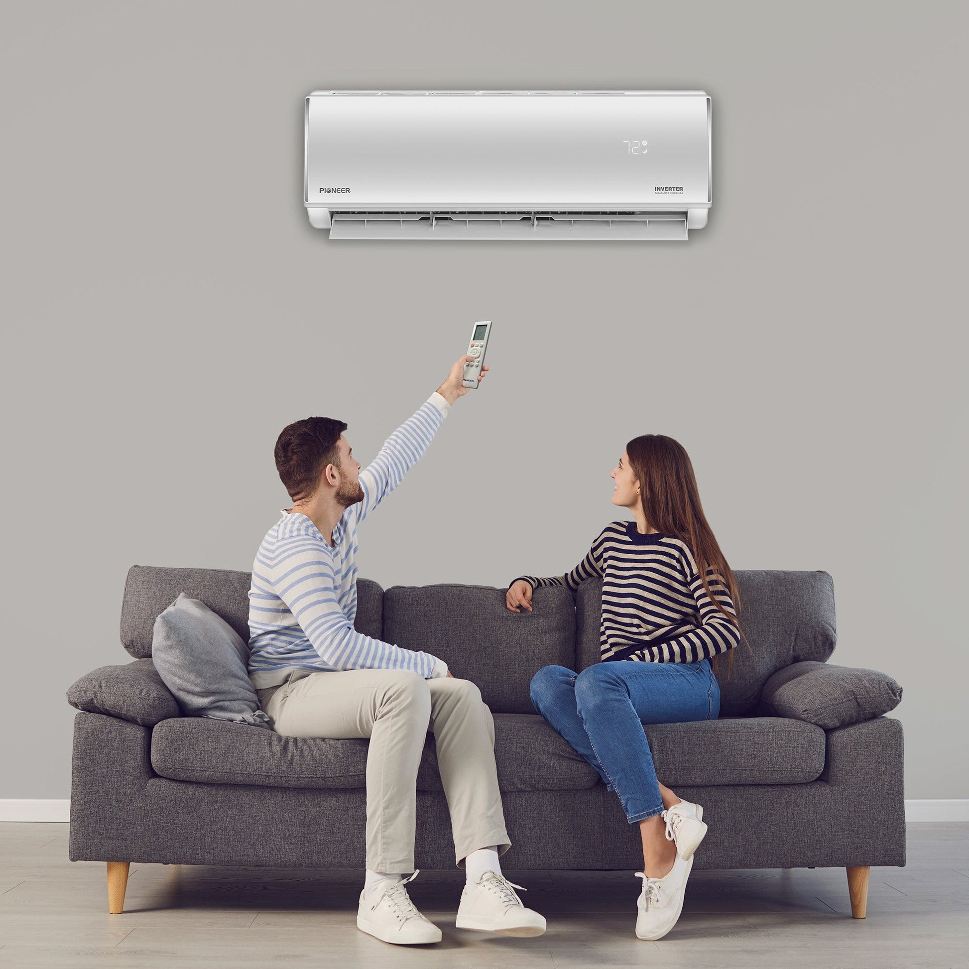 Man and woman sitting on a couch using a remote control to operate an air conditioner.